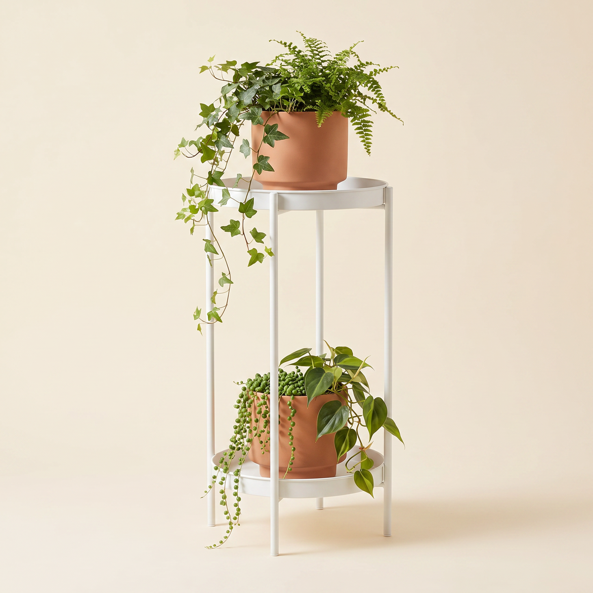 Modern 2-tier white metal plant stand with terracotta ceramic pots and trailing plants, studio shot